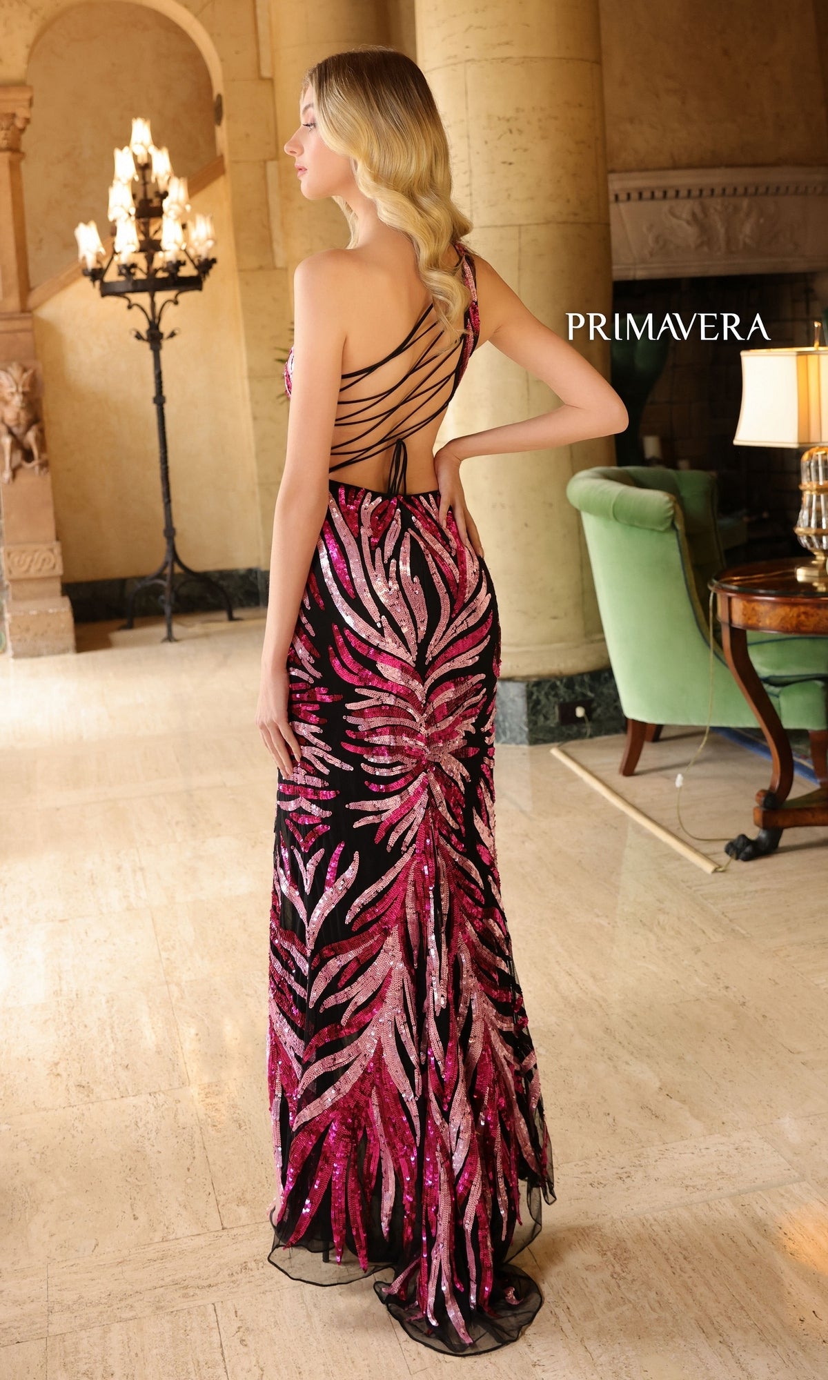 A woman stands indoors wearing the One-Shoulder Primavera Long Beaded Prom Dress 4119—a floor-length black and pink sequin gown with a strappy open back.